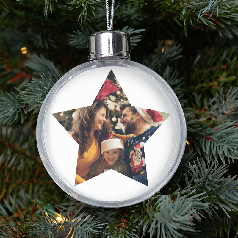 Decorative Christmas ornament with a star-shaped cutout featuring a family photo, hanging on a Christmas tree.